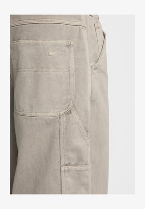Béžové nohavice typu cargo s textúrovanou tkaninou, s bočnou vreckom a malým vyšívaným logom Nike na zadnom vrecku.