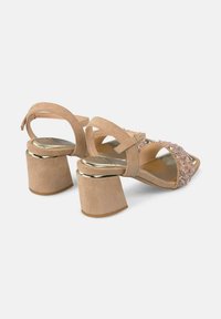 Sandalias de tacón bloque en color beige con la parte trasera abierta, que presentan un diseño decorativo de gemas rosas y transparentes en la correa delantera, y una suave textura de ante.