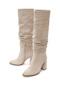 Beżowe zamszowe kozaki do kolan z luźnym cholewką, kwadratowym noskiem, masywnym obcasem i bocznym zamkiem błyskawicznym. Gładka faktura i minimalistyczny design.