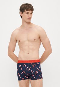 Cuecas boxer masculinas em azul-marinho com padrão de bastão de doce. Cós vermelho com texto "HAPPY". Tecido suave com design ajustado.