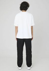 T-shirt en coton blanc avec une coupe décontractée, des manches courtes et un col rond. Associé à un pantalon noir et des baskets blanches. Design épuré.