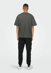 Mørk grå oversized t-shirt med korte �ærmer og rund halsudskæring, stylet med sorte cargo bukser med sidelommer og elastiske manchetter. Hvide sneakers.