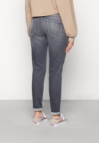Jeans de mezclilla gris con un corte ajustado, cuatro bolsillos y puños enrollados, combinados con zapatillas de color claro. Tejido suave y texturizado.