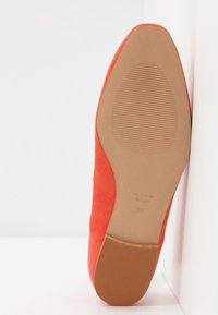 Vue de dessous d'une chaussure plate rouge montrant sa semelle avec des motifs antidérapants et la taille 37 marquée "Made in Spain".