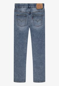 Vaqueros de mezclilla azul claro con cintura elástica, que presentan dos bolsillos traseros y un parche de cuero grabado de la marca en la cintura.