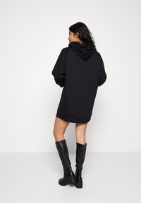 Schwarzer übergroßer Hoodie mit Kapuze, gerippten Bündchen und Saum. Getragen mit knielangen schwarzen Lederstiefeln. Einfaches Design und Textur.