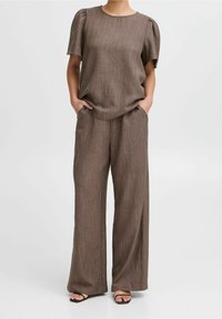 Brun tvådelad outfit bestående av en kortärmad topp med texturerad tyg och vida byxor. Båda har fina vertikala ränder och fickor.