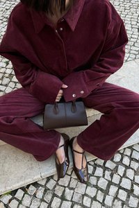 Camisa de pana burdeos de corte Oversize y pantalones, combinados con un bolso de cuero marrón y zapatos marrones brillantes con diseño calado.