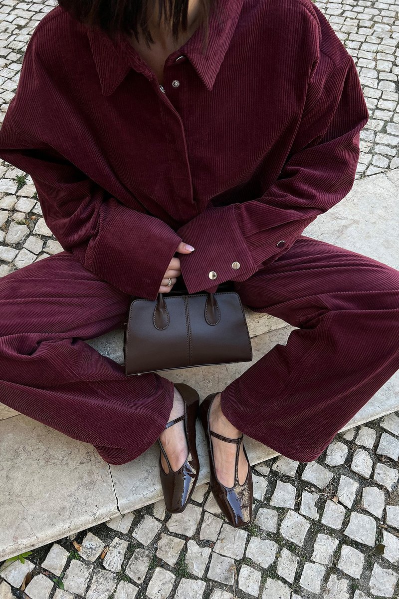 Camisa de pana burdeos de corte Oversize y pantalones, combinados con un bolso de cuero marrón y zapatos marrones brillantes con diseño calado.