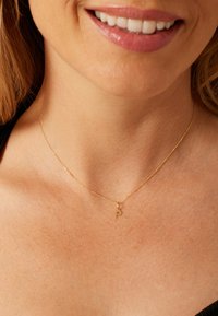 Collier ton or avec une chaîne fine et un petit pendentif en forme de lettre « P », reposant sur la peau au niveau du cou. Design simple et délicat.