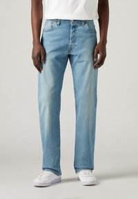 Jeans in denim azzurro con taglio dritto, cinque tasche e leggere sfumature. Indossati con sneakers bianche e una semplice camicia bianca.