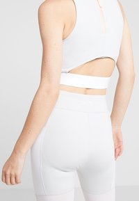 Sostenedor deportivo blanco con diseño de espalda cortada, combinado con leggings blancos de cintura alta que exhiben un sutil logo y detalles de costura.