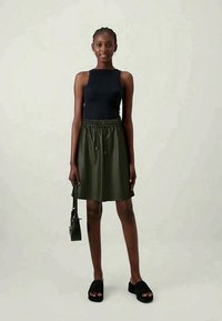 Μαύρη αμάνικη μπλούζα, ελιά πράσινη φούστα με λάστιχο στη μέση, μαύρες επίπεδες σανδάλια και μια μικρή μαύρη τσάντα. Απλές, καθαρές γραμμές και ουδέτερα χρώματα.