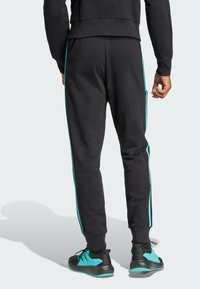 Black sweatpants with turquoise side stripes, made of soft fabric. Elastic waistband and cuffed ankles. Pocket detail on the side.