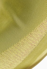 Zelená textilie s jemně žebrovanou strukturou, zdobená třásněmi na okraji. Materiál se zdá být měkký a elastický, což zvyšuje vizuální hloubku designu.