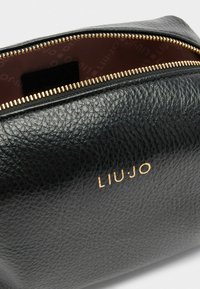 Pouch in pelle nera texturizzata con zip dorata e logo del marchio "LIU•JO" stampato in oro. L'interno presenta una morbida fodera in tessuto.