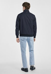 Granatowa kurtka bomberka z wysokim kołnierzem, żebrowanymi mankietami i pasem. Charakteryzuje się minimalistycznym wzornictwem, lekkim materiałem oraz detalami na plecach.