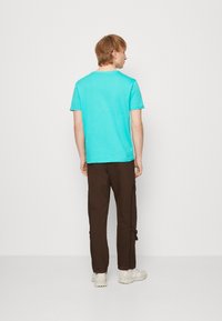 Türkises Baumwoll-T-Shirt mit Rundhalsausschnitt, kombiniert mit braunen Cargo-Hosen mit Seitentaschen und hellen Sneakers.