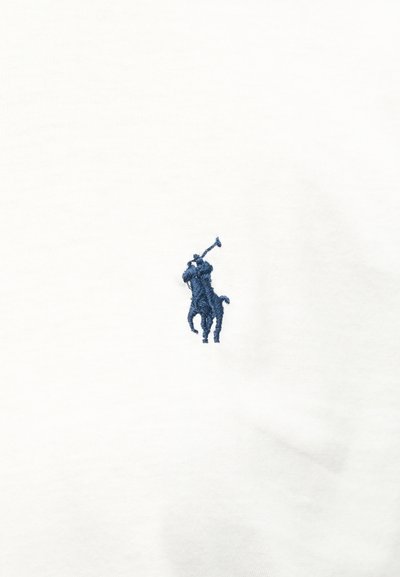 Μικρό σκούρο μπλε κεντημένο λογότυπο με παίκτη πόλο επάνω σε άλογο που κρατάει υψωμένο μαλέτι, σε λευκό ύφασμα.