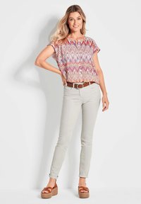 Haut à manches courtes à motifs en rose et bleu, associé à un pantalon gris clair ajusté et une ceinture marron. Des sandales compensées avec une semelle tissée sont portées.