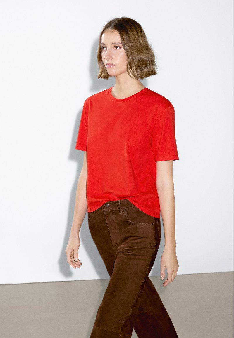 T-shirt in cotone rosso con maniche corte e collo rotondo. Abbinato a pantaloni in suede marrone, con una texture liscia e tasche frontali.