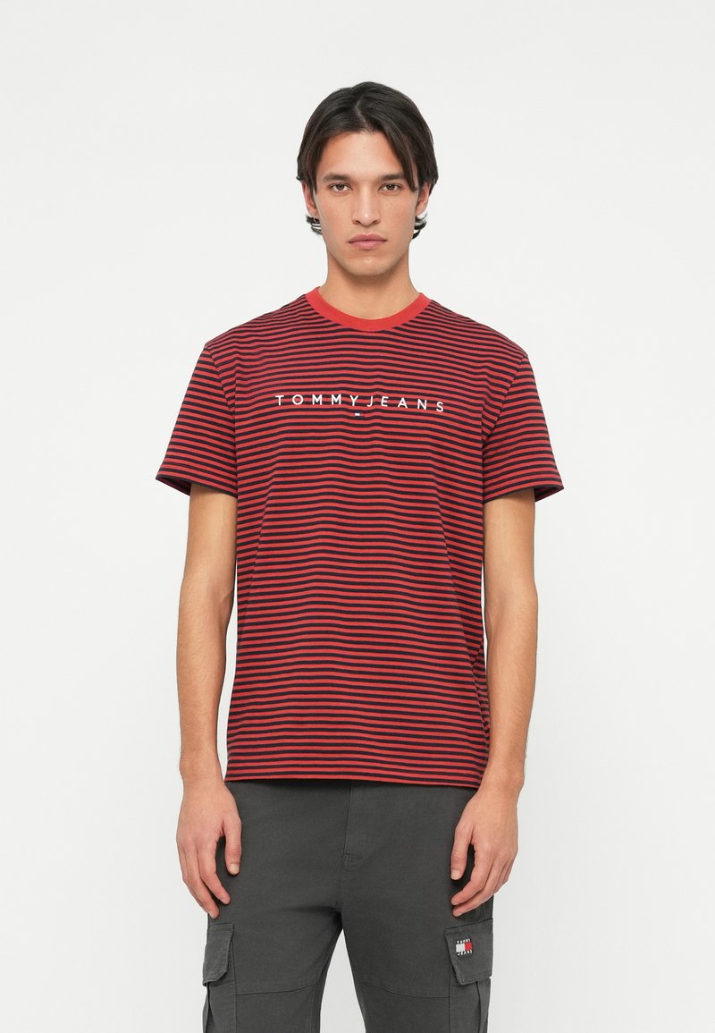Rød og marineblå stripete T-skjorte med rund hals og kontrasterende rød krage. Har hvit "TOMMY JEANS" logo over brystet.