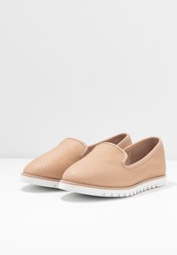 Scarpe beige slip-on con una superficie testurizzata che ricorda piccole squame, dotate di una suola in gomma bianca e una punta arrotondata.