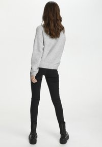 Grauer Strickpullover mit lockerem Schnitt, kombiniert mit figurbetonten schwarzen Jeans und schwarzen Stiefeletten mit einer groben Sohle. Rückansicht.