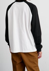 Langärmeliges Raglan-T-Shirt mit weißem Körper und schwarzen Ärmeln, aus weichem Stoff gefertigt und mit einfachem Design. Die Rückseite ist einfarbig.