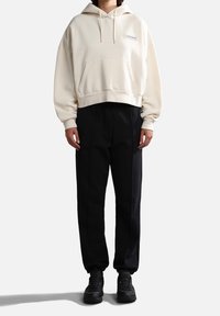 Krämfärgad cropped hoodie med en framficka och dragsko på huva, kombinerad med högmidjade svarta byxor och mörka sneakers.