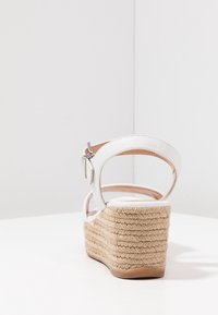 Valkoiset espadrille-korkokengät, joissa on kudottu juuttikorko, nilkkaremmi ja sileä nahkapeite. Varustettu säädettävällä soljella.