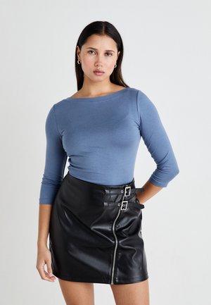 Long-sleeve blue top in soft fabric paired with a black faux leather mini skirt featuring a front zipper and two buckle accents.
