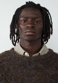 Braun strukturierter Pullover aus fuzzy Material über einem karierten Hemd. Der Kragen blitzt hervor und fügt dem Lagenlook Kontrast hinzu.