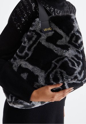 Persona con suéter negro con lentejuelas sostiene un bolso grande de imitación de piel con patrón en negro y gris de Liu Jo, con correa de cuero.