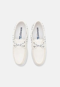 Weiße Lederschuhe im Bootsstil mit marineblauen Akzenten, runder Zehenform, Schnürung durch metallene Ösen und kontrastierendem Nähten. Texturiertes Fußbett sichtbar.