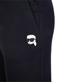 Granatowe dresy z gumowym naszywką przedstawiającą postać w okularach przeciwsłonecznych. Materiał jest miękki o gładkiej fakturze. Dodatkowe detale po bokach.