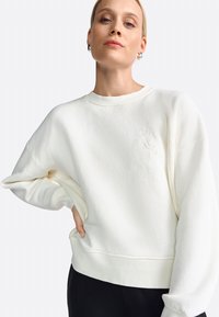 Weißes Sweatshirt mit Rundhalsausschnitt, überschnittenen Schultern, gerippten Bündchen und gesticktem Detail "ROYAL" auf der Vorderseite. Weicher Stoff.