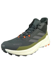 Szare i oliwkowo-zielone buty do biegania z materiałem Gore-Tex, teksturową powierzchnią, pomarańczowymi akcentami i białą, solidną podeszwą zapewniającą przyczepność.