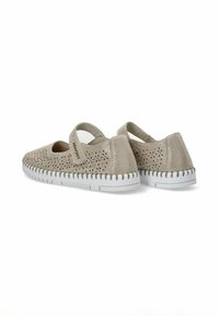 Zapatos perforados beige con una correa, que cuentan con una suela blanca y texturizada. La vista trasera resalta el diseño único y los materiales utilizados.