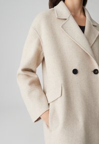 Beige wollen blend double-breasted jas met een reverskraag, twee voorzakken en donkere knopen. Zachte textuur met een getailleerd ontwerp.