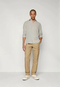 Camisa de botão quadriculada em bege e branco, combinada com calças cargo em caqui claro. Footwear consiste em ténis de lona brancos com uma sola texturizada.