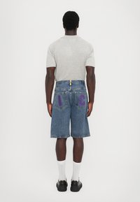 Rdeče jeans kratke hlače z ravnim krojem, z vijoličnimi izvezenimi črkami "I" in "C" na zadnjih žepih. Siva majica s kratkimi rokavi.