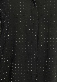 Top in tessuto nero con un motivo a pois di piccoli dettagli argentati, con una texture liscia e una leggera lucentezza.