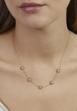 Goldkette mit fünf blumenförmigen Anhängern, jeder mit einem zentralen Edelstein und dekorativen Perlenakzenten, die auf nackter Haut liegt.