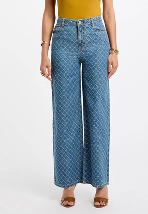 Weite Denim-Jeans in Hellblau mit einem Rautenmuster, hoher Taille, Seitentaschen und kontrastrichtiger Nähte. Kombiniert mit braunen Sandalen.