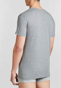 Maglietta grigia a maniche corte con scollatura tonda, realizzata in tessuto morbido, indossata con pantaloni corti grigi chiari, vista da dietro.