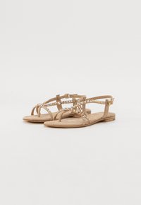 Flate sandaler i tan med dekorative rhinestener, med flere stropper og justerbar spenne. Mykt semsket materiale, minimalistisk design.