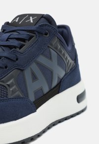 Baskets bleu marine avec tige en mesh et suède, logo gris proéminent, accents texturés, semelle intermédiaire blanche et semelle extérieure en caoutchouc noir.