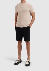 Beige short-sleeved knitted t-shirt with a textured finish, paired with black tailored shorts and black loafers with white accents.
