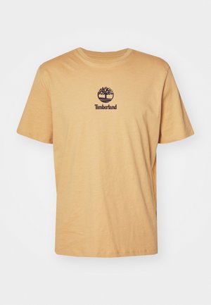 Μπεζ κοντομάνικη μπλούζα Timberland με μαύρο λογότυπο δέντρου και όνομα της εταιρείας στο κέντρο του στήθους, σε απλό φόντο.